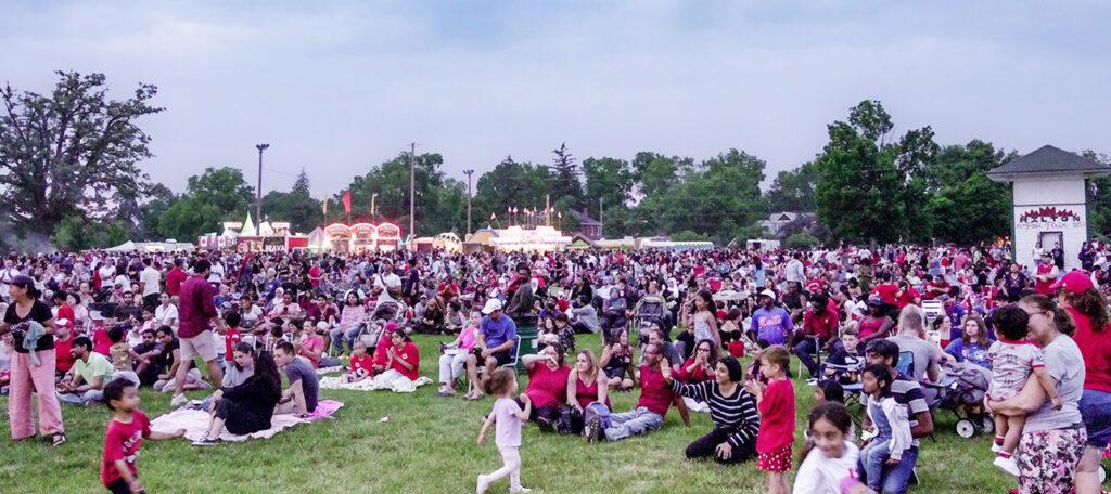 A large group of people gathered, sitting on the grass, for the Canada Day celebration in Milton, 2023.